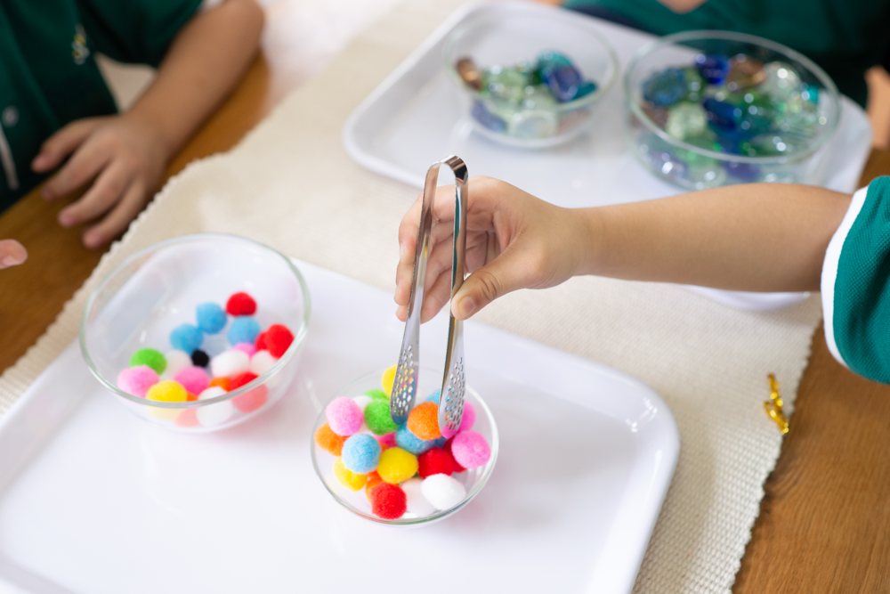 A child using tweezers to pick up pom-poms – a Montessori activity for fine motor skills and focus
